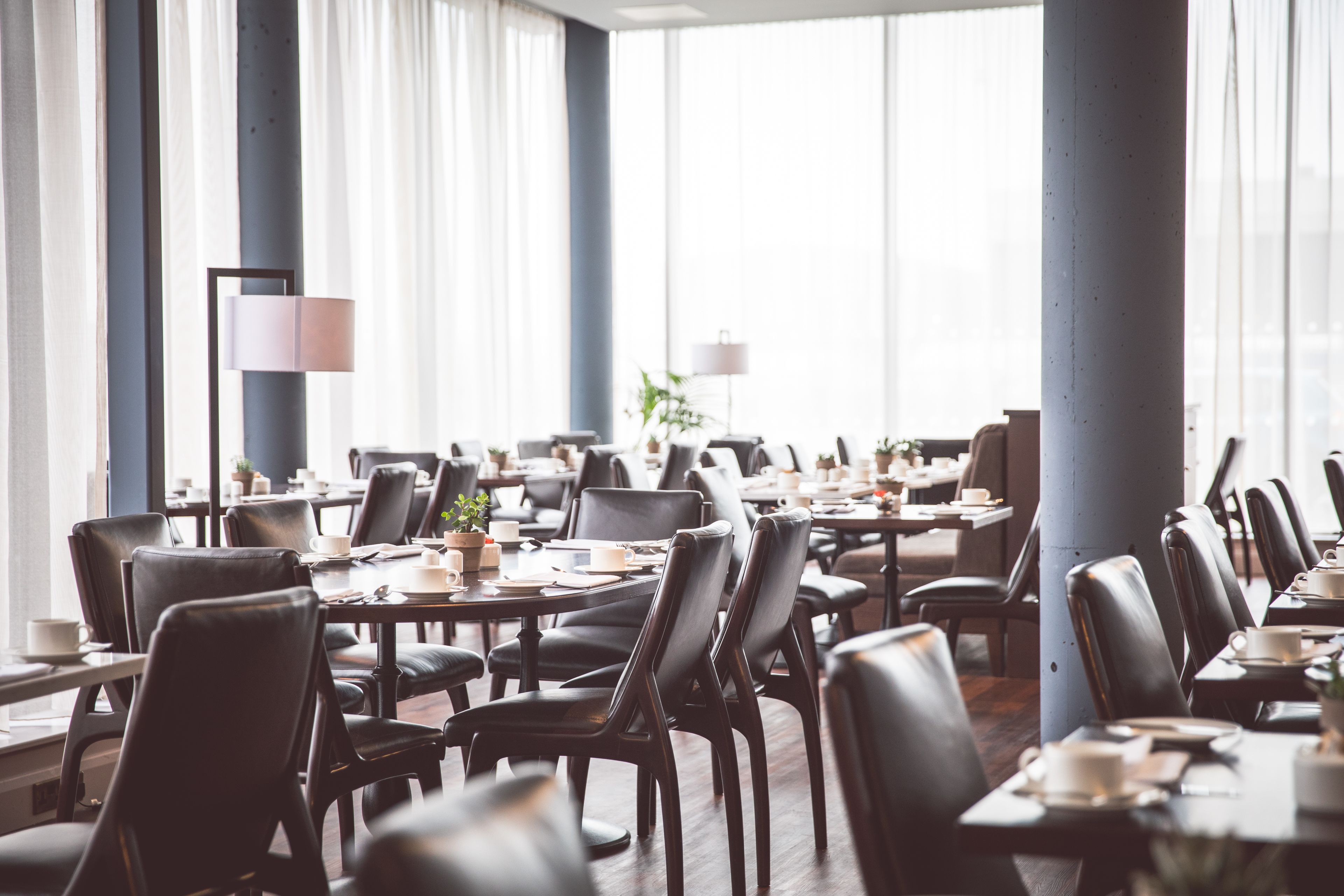 A spacious dining area with multiple tables and chairs, large windows, and a modern interior design.