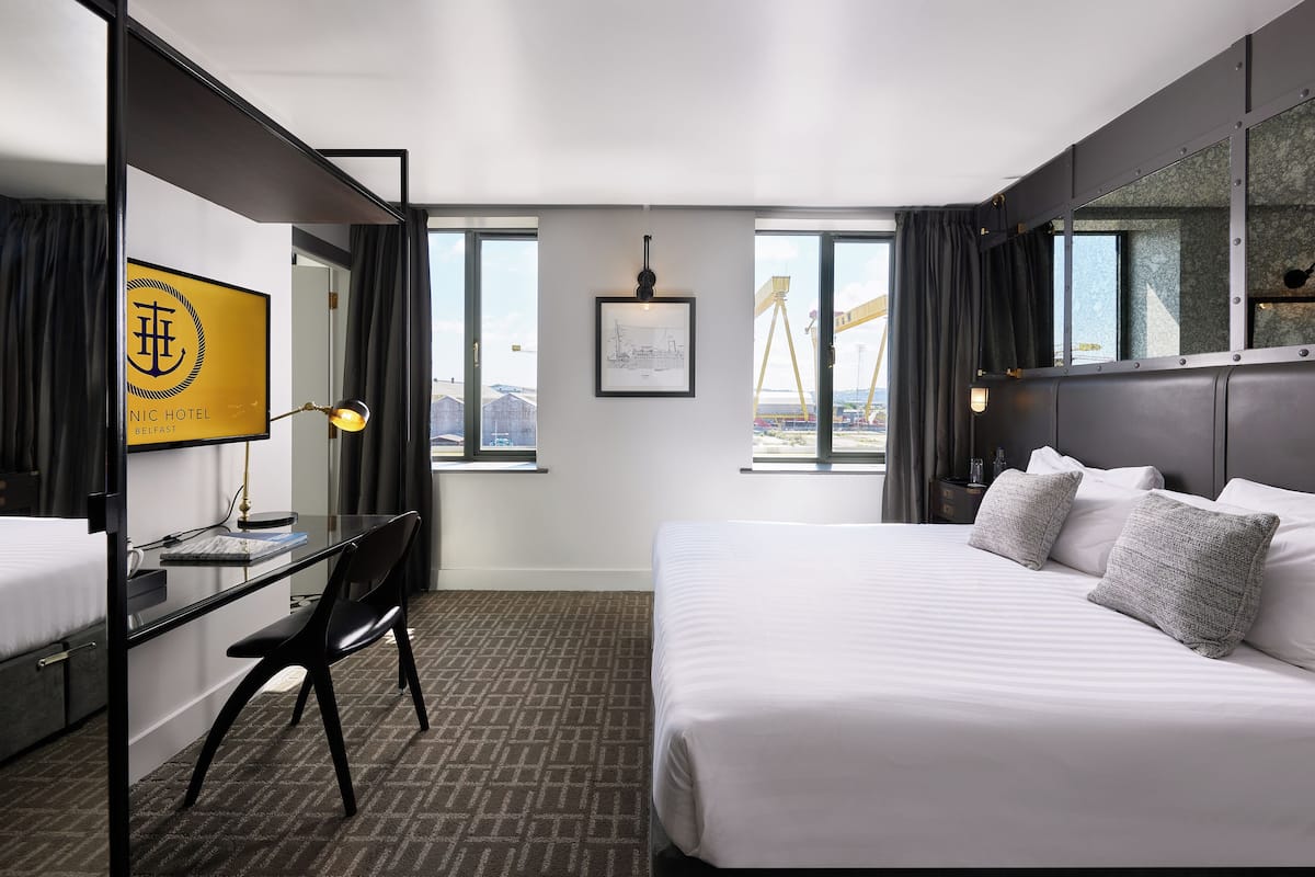 Una habitación de hotel moderna con una cama grande, un escritorio y una silla. Hay una ventana que ofrece vistas a una grúa fuera.