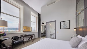 Une chambre d’hôtel avec un grand lit, un bureau, une chaise, une coiffeuse et une fenêtre donnant sur la ville.