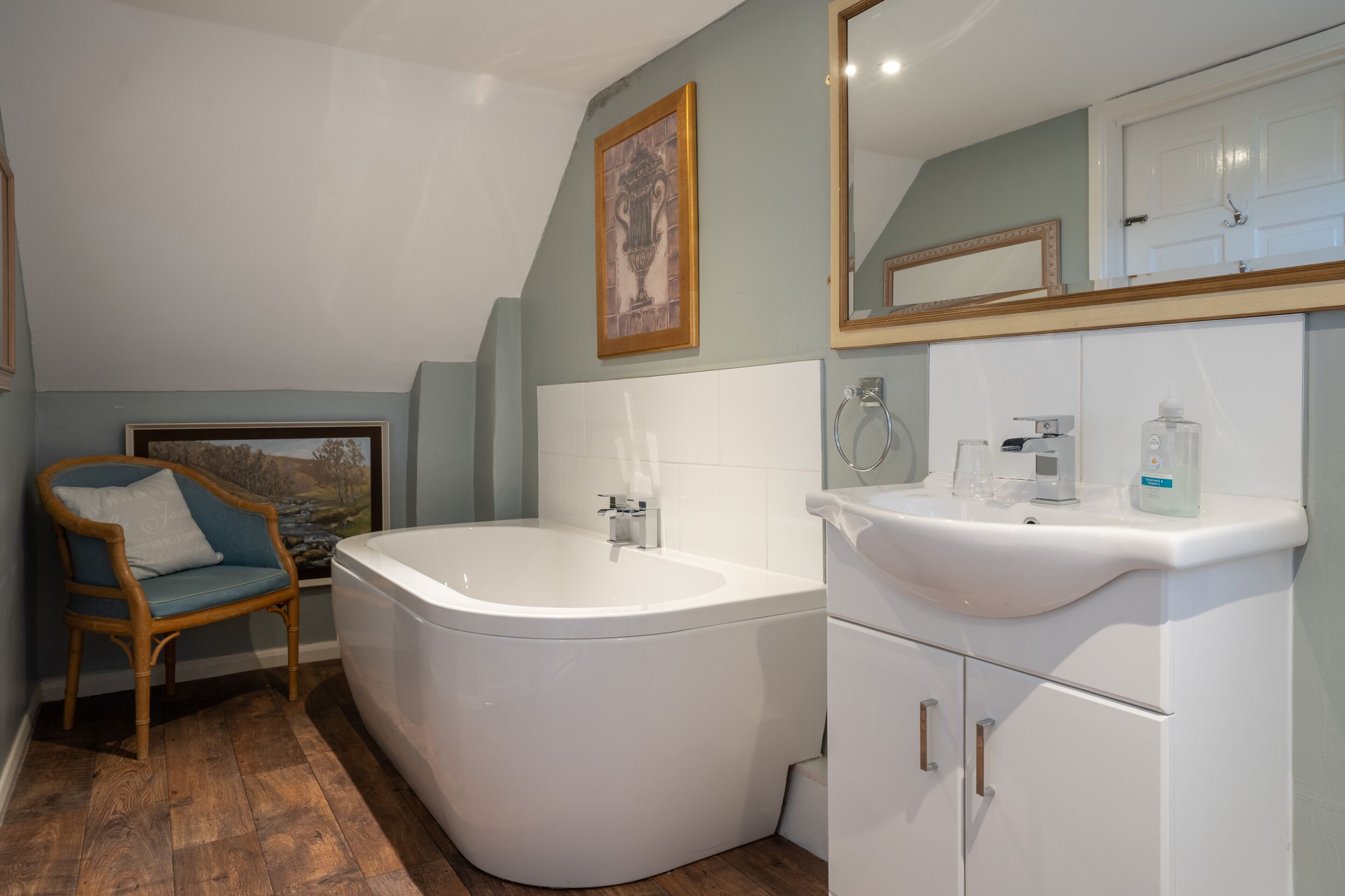 Une salle de bain avec une baignoire sur pieds, un lavabo blanc et une chaise en bois.