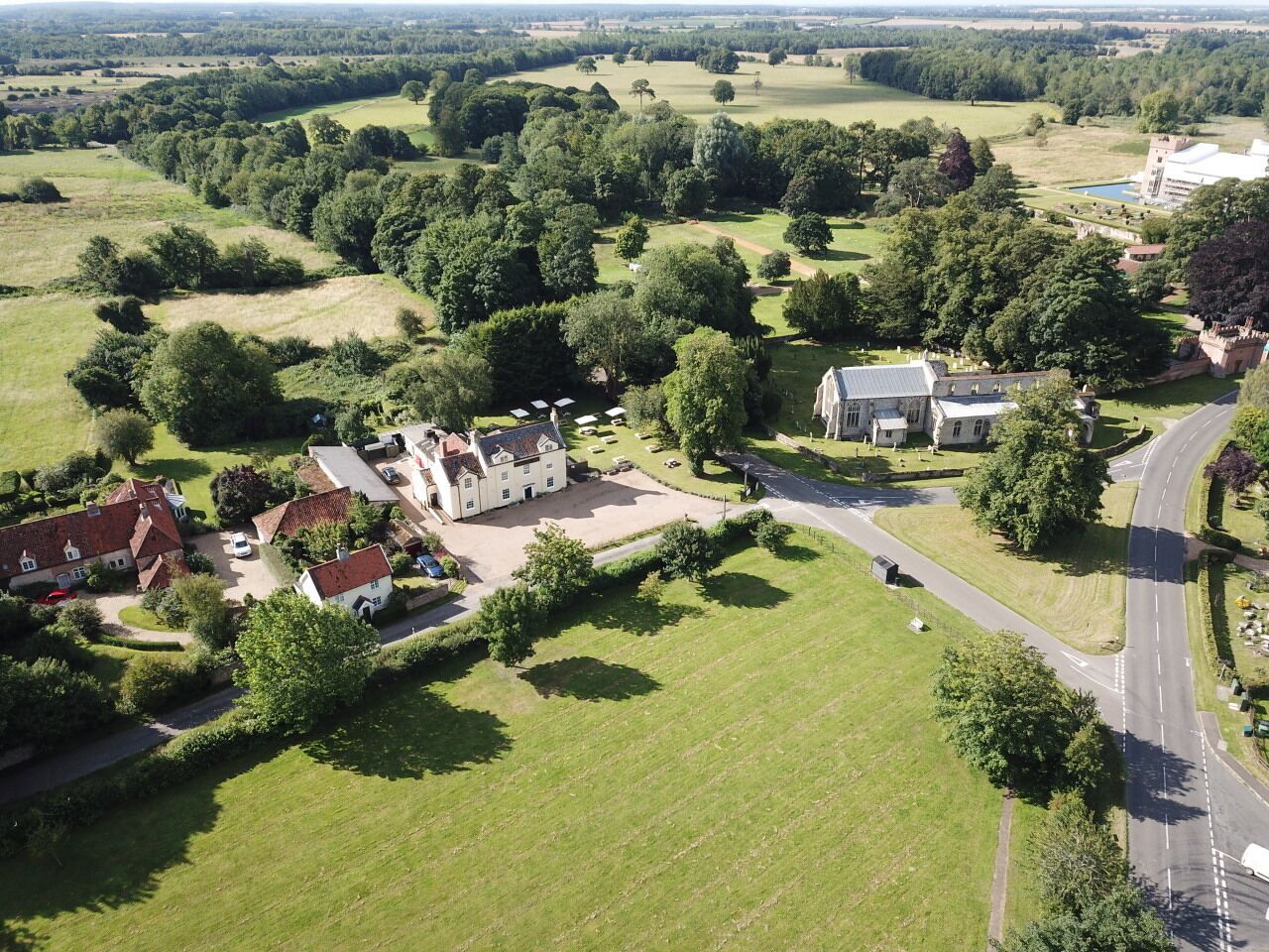 Vue aérienne d’un domaine rural comprenant plusieurs bâtiments, notamment une grande maison avec un jardin, une maison plus petite et un bâtiment blanc avec un toit rouge.