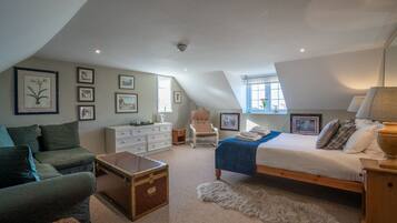 A bedroom with a loft-style ceiling, a bed with a blue blanket, a dresser, a chair, and framed pictures on the walls.