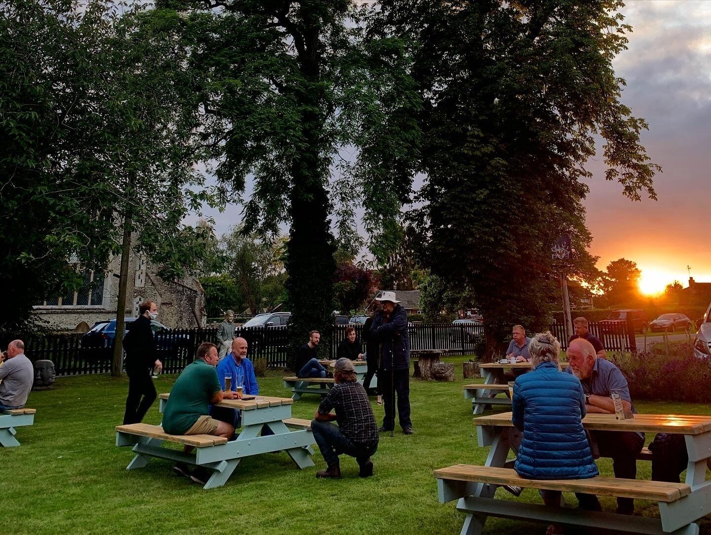 A group of people seated at picnic tables outdoors during sunset.