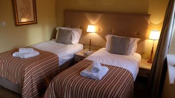 Habitación de hotel con dos camas individuales, cada una con colcha a rayas y almohada blanca. Hay lámparas de noche y un cuadro en la pared.