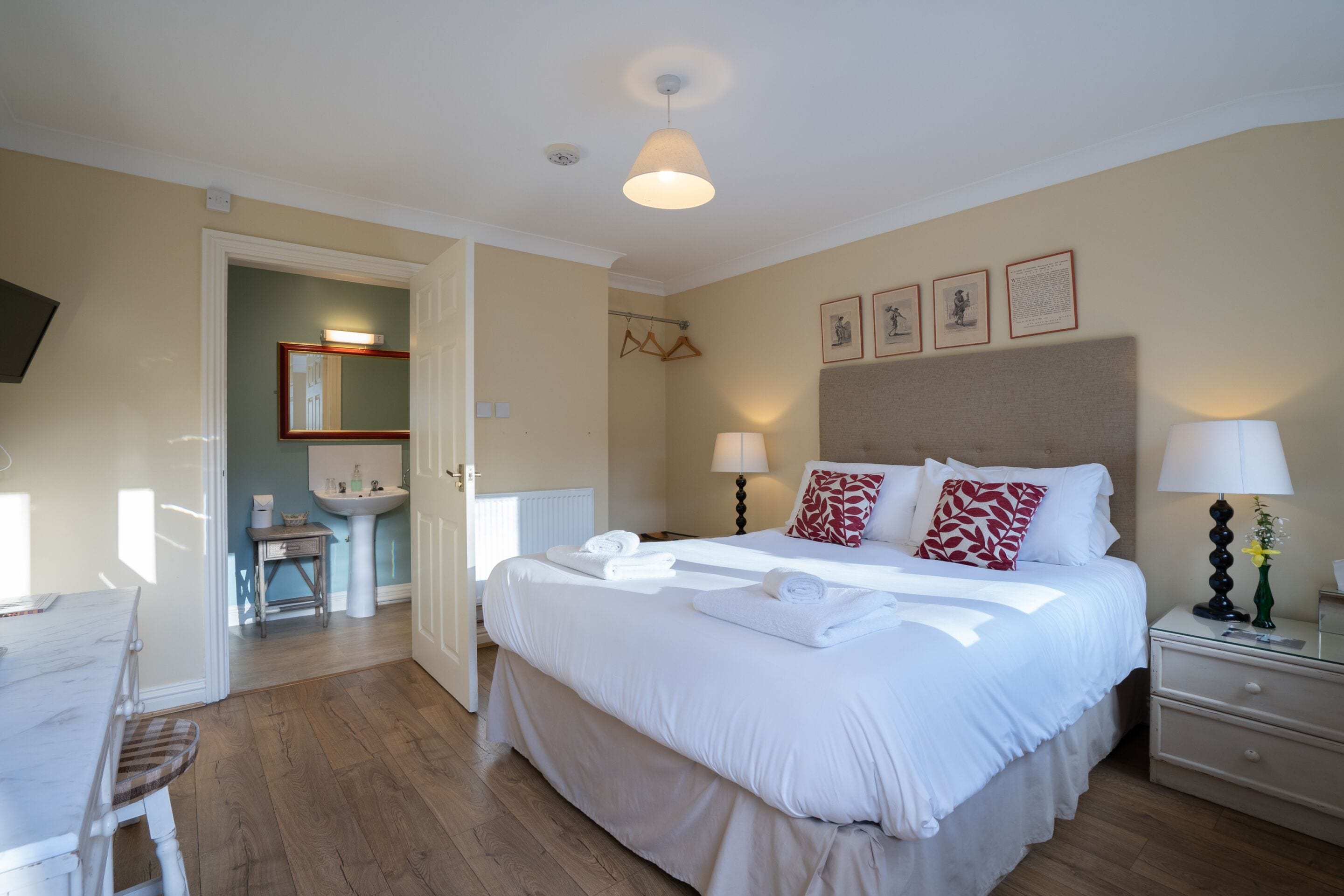 Une chambre d’hôtel avec un grand lit, des lampes de chevet, une table de chevet, une chaise, un bureau et une salle de bain visible à travers une porte ouverte.