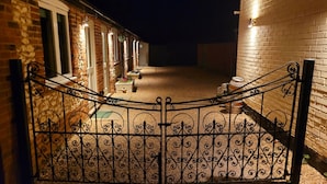 A gated courtyard with a brick wall, a metal gate, and a pathway leading to a building with windows and a small garden area. - Bedingfeld Arms (King's Lynn)