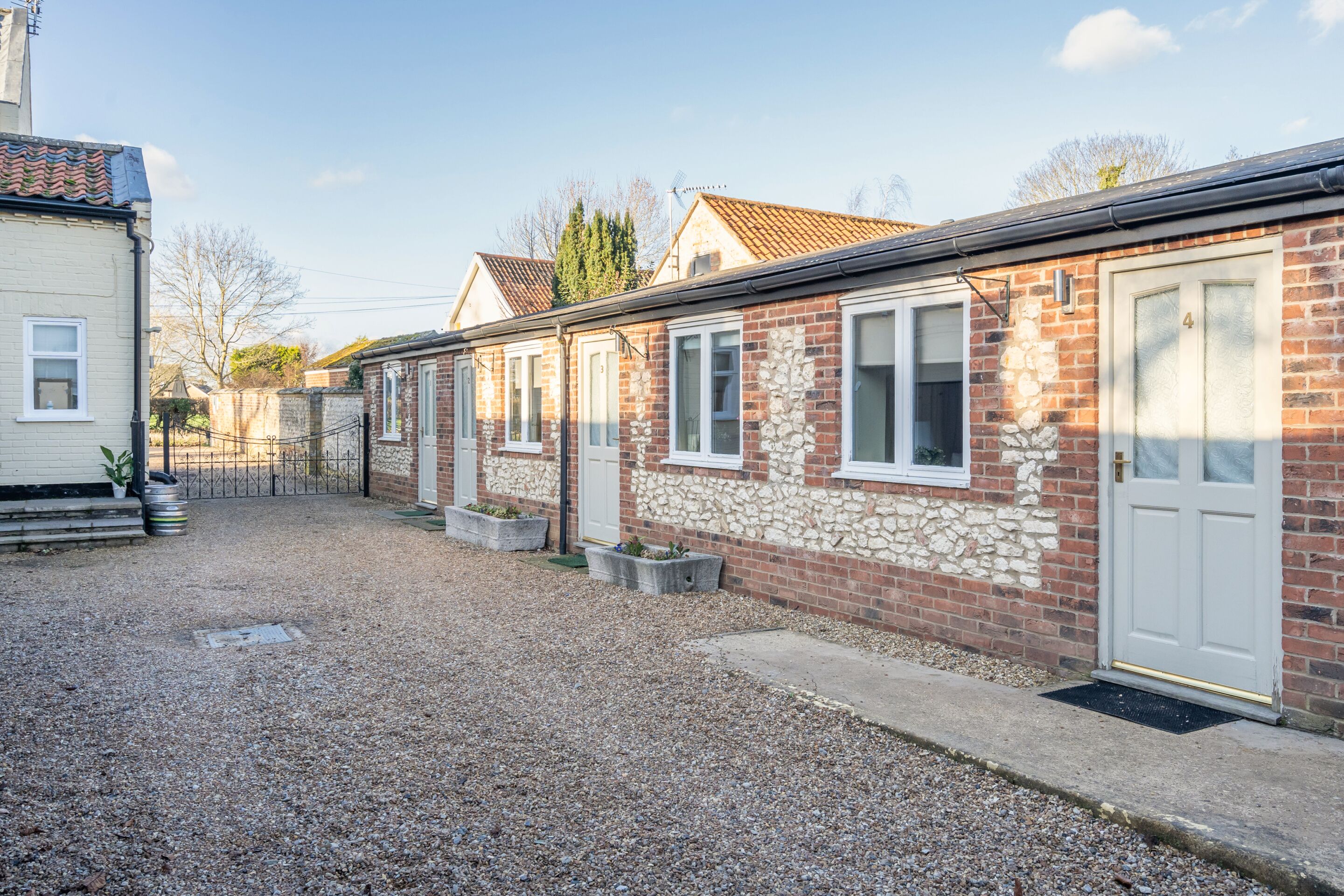 A row of brick houses with white doors, a gravel driveway, and a metal fence.