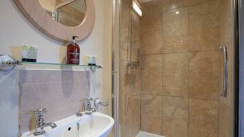 A bathroom with a glass-enclosed shower, a white sink with two faucets, and a round mirror above the sink.