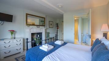 A hotel room with a large bed, a fireplace, a television, and a bathroom visible through an open door.
