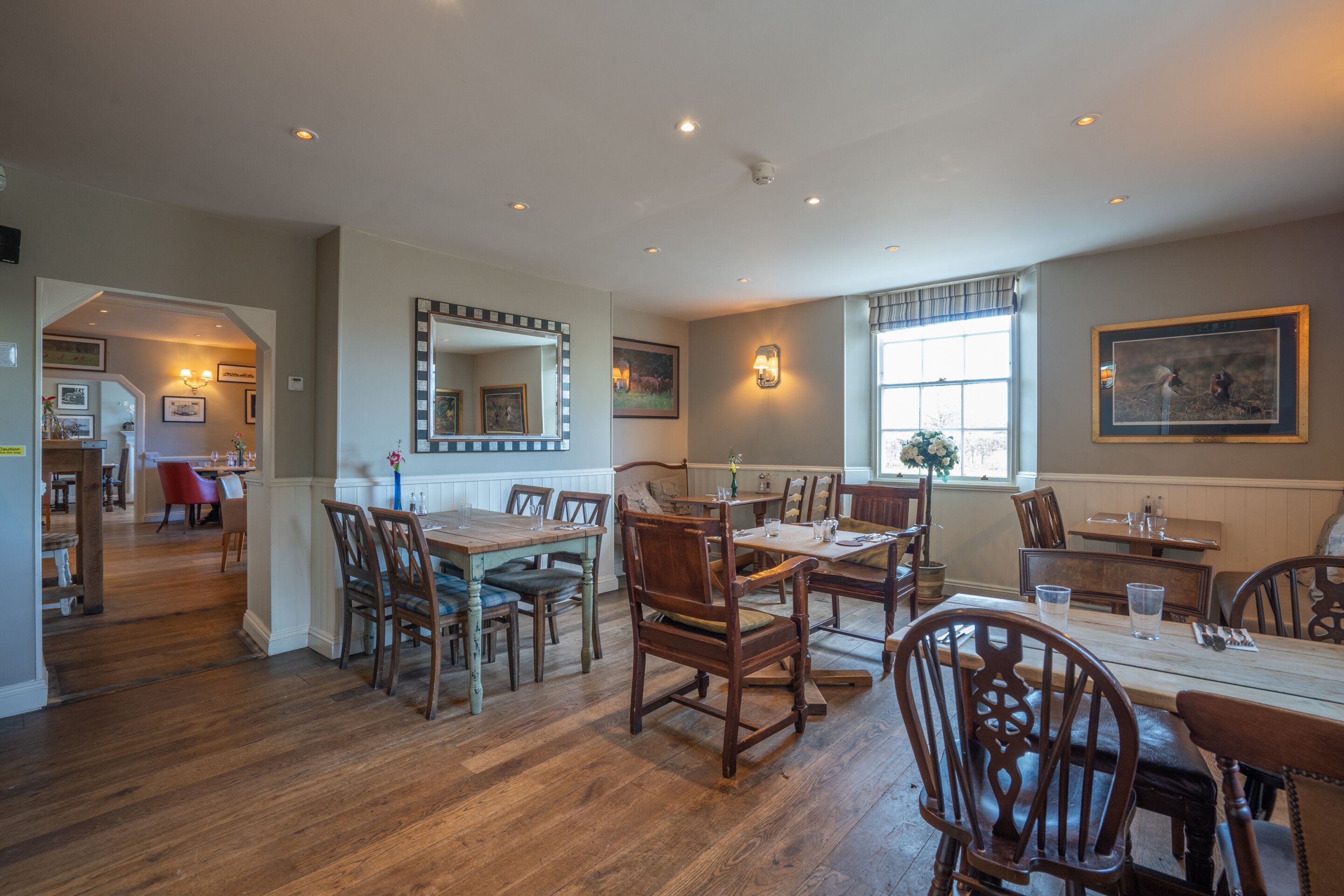 A dining area with wooden tables and chairs, a large mirror, and framed artwork on the walls.