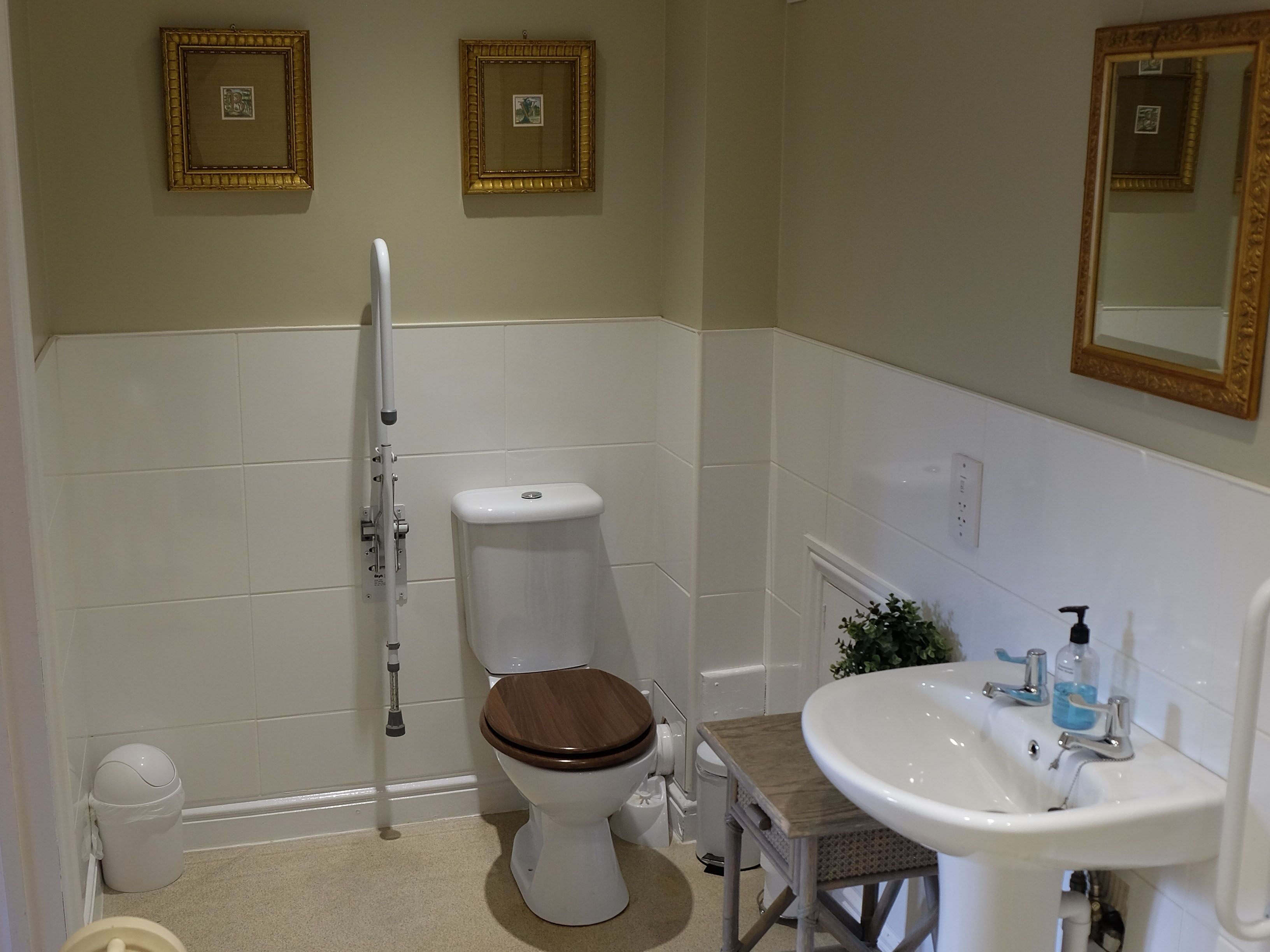 A bathroom with a toilet, bidet, sink, and two framed pictures on the wall.