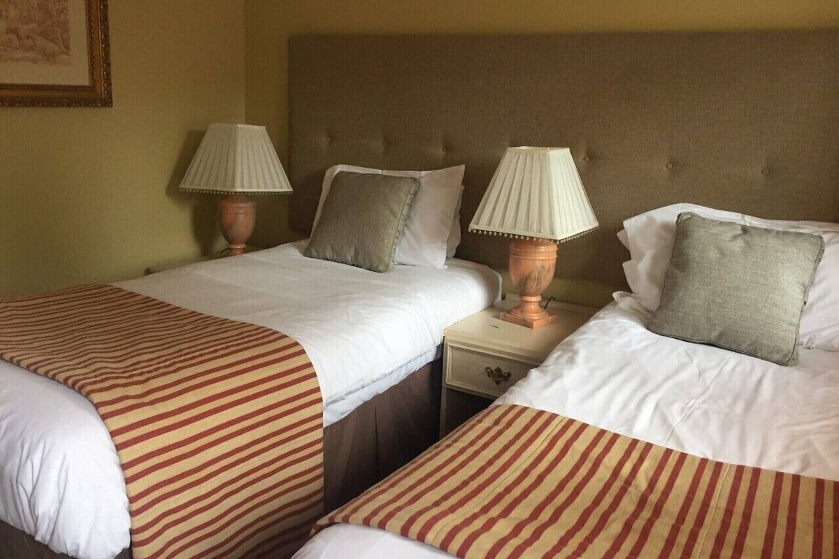 Quarto de hotel com duas camas, cada uma com colcha listrada, duas luminárias de cabeceira e uma mesa de cabeceira de madeira.