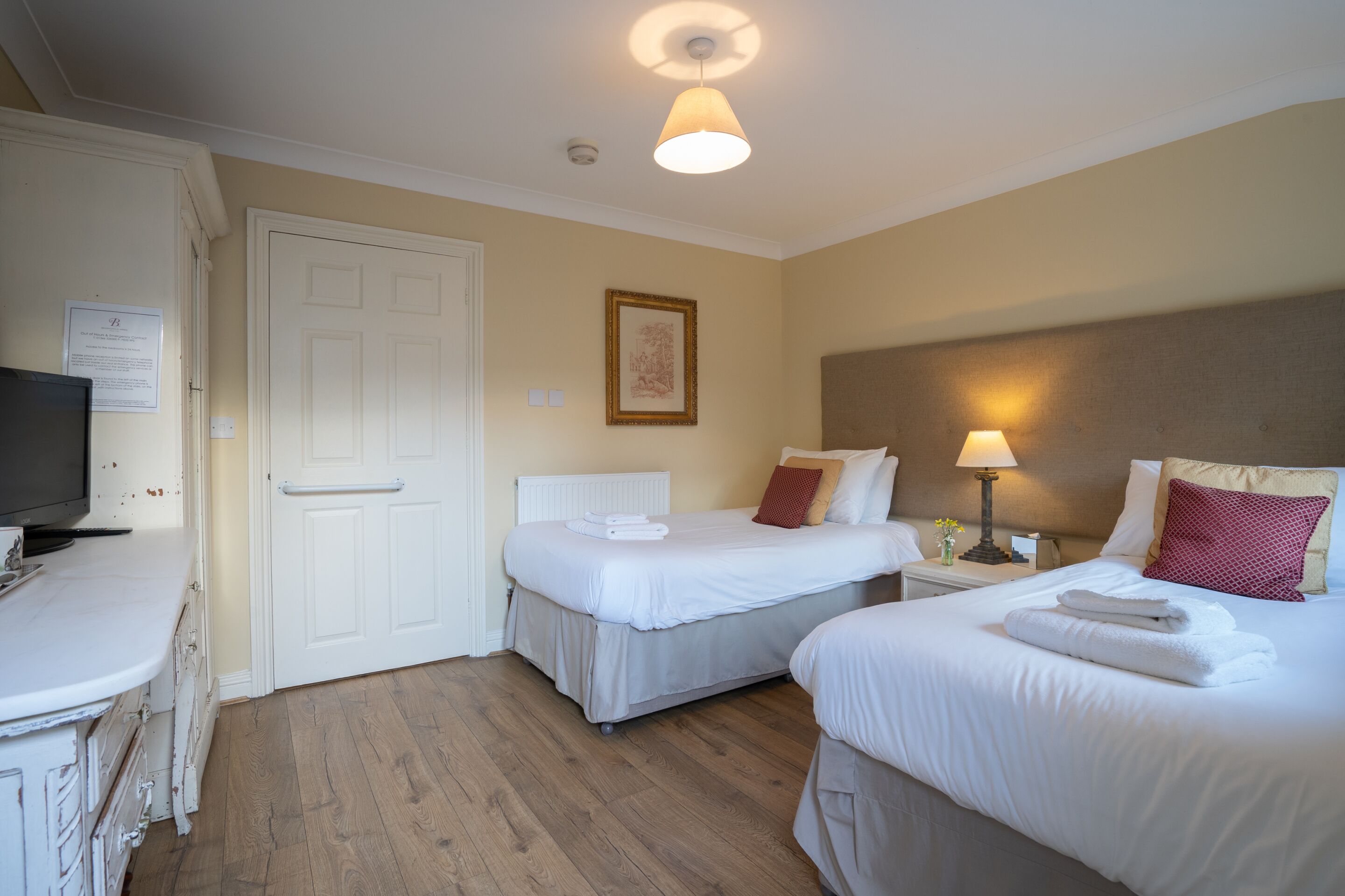 A hotel room with two beds, a television, a white dresser, and a door.