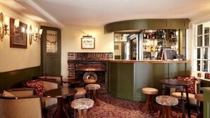 A cozy pub with a brick fireplace, wooden furniture, and a bar area with bottles. - The Stag and Huntsman (Henley-on-Thames)
