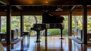 Un piano de cola en una habitación amplia con ventanas grandes que dan a un jardín exuberante.