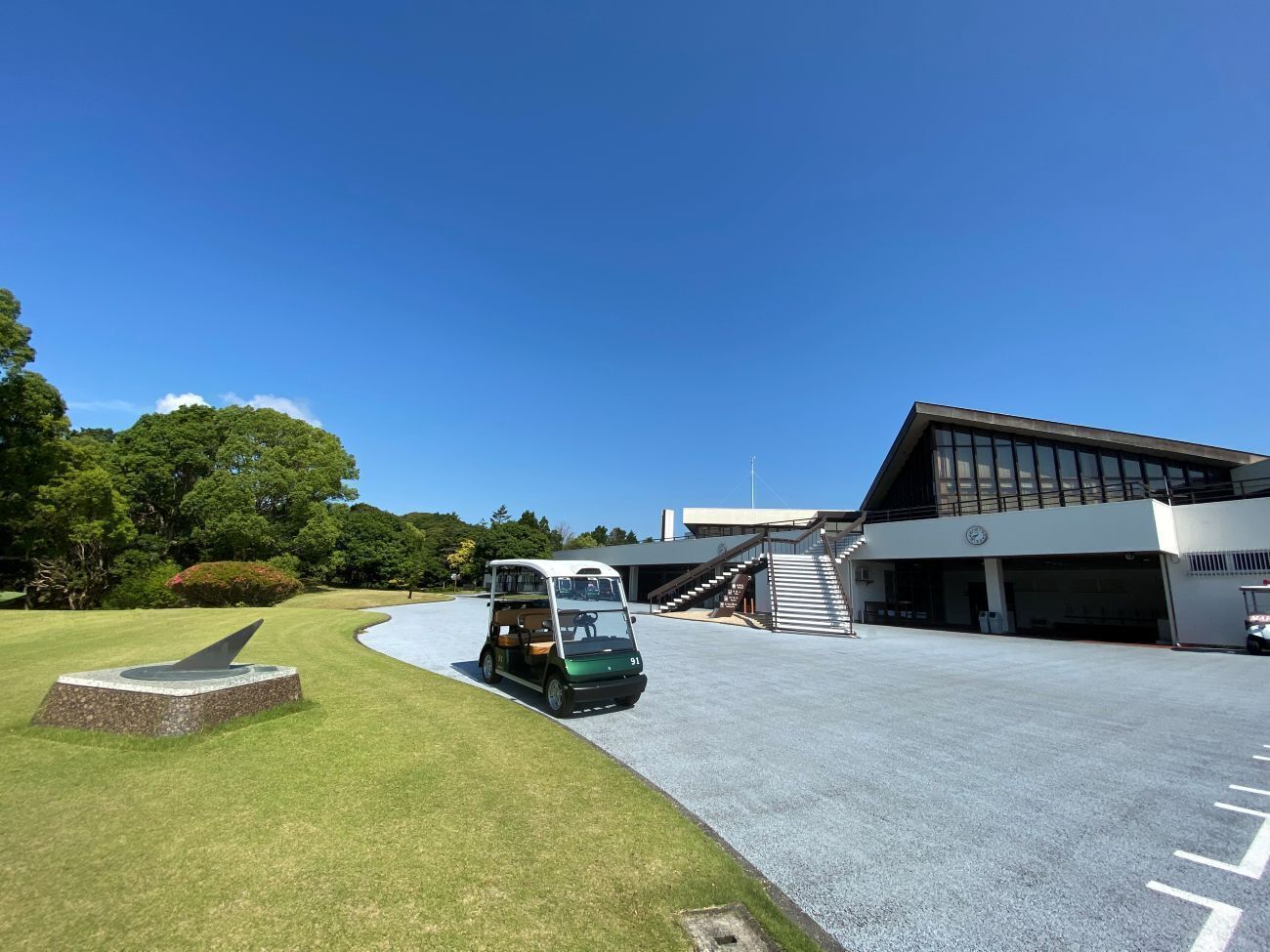 A parking area with a green vehicle, a building with a modern design, and a clear sky.