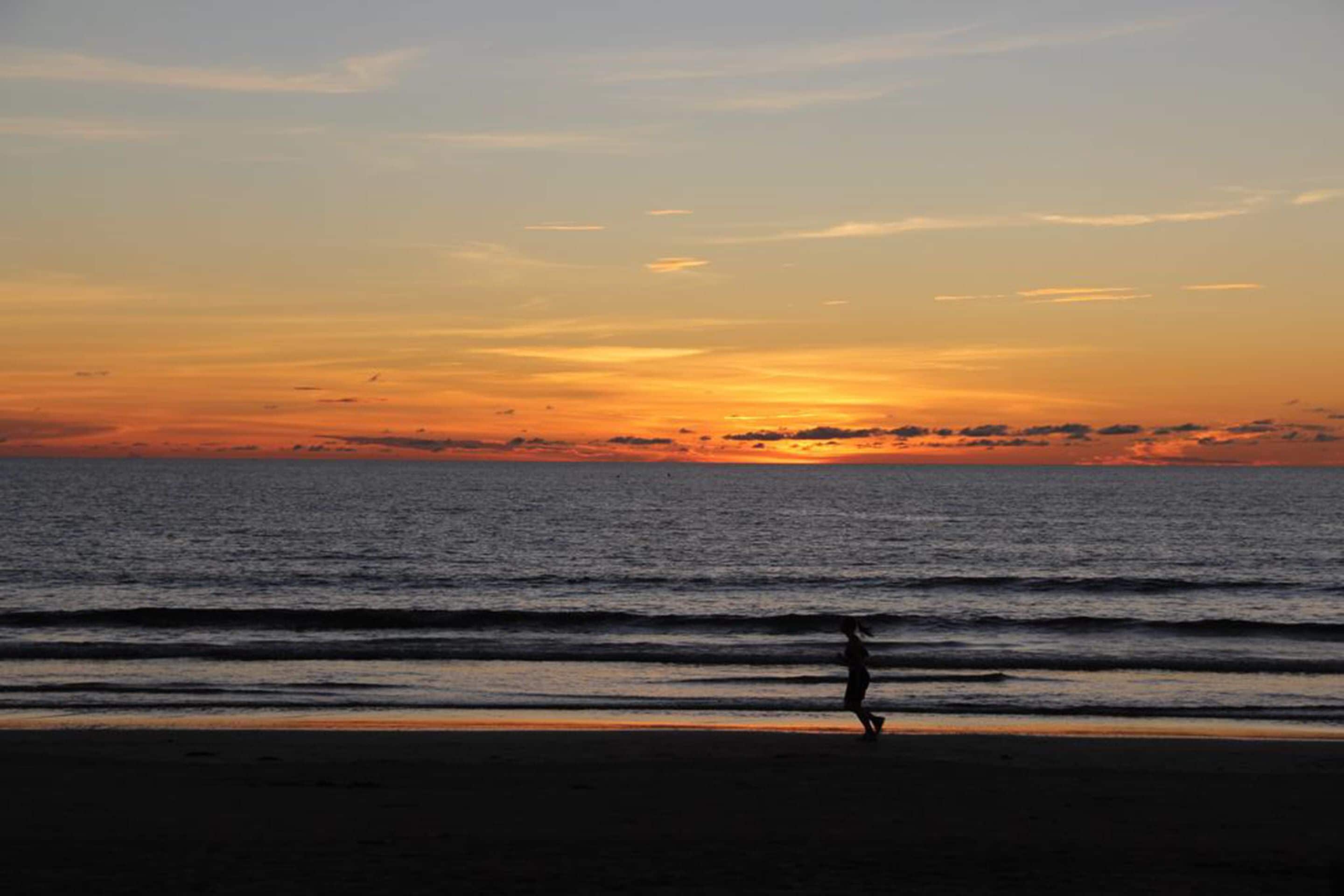 A beach at sunset with waves and a silhouette of a person.