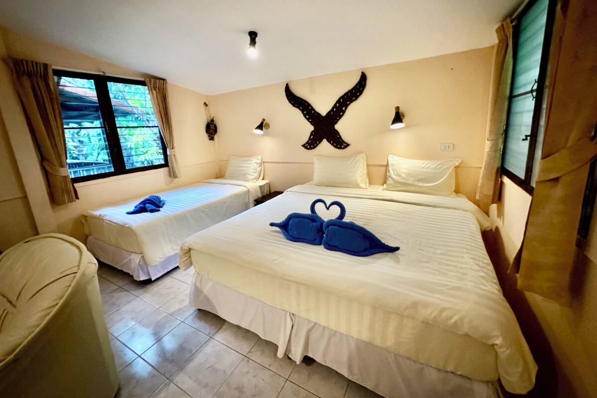 A hotel room with two single beds, a large bed, a window with curtains, a wall-mounted light fixture, and a decorative wall piece.