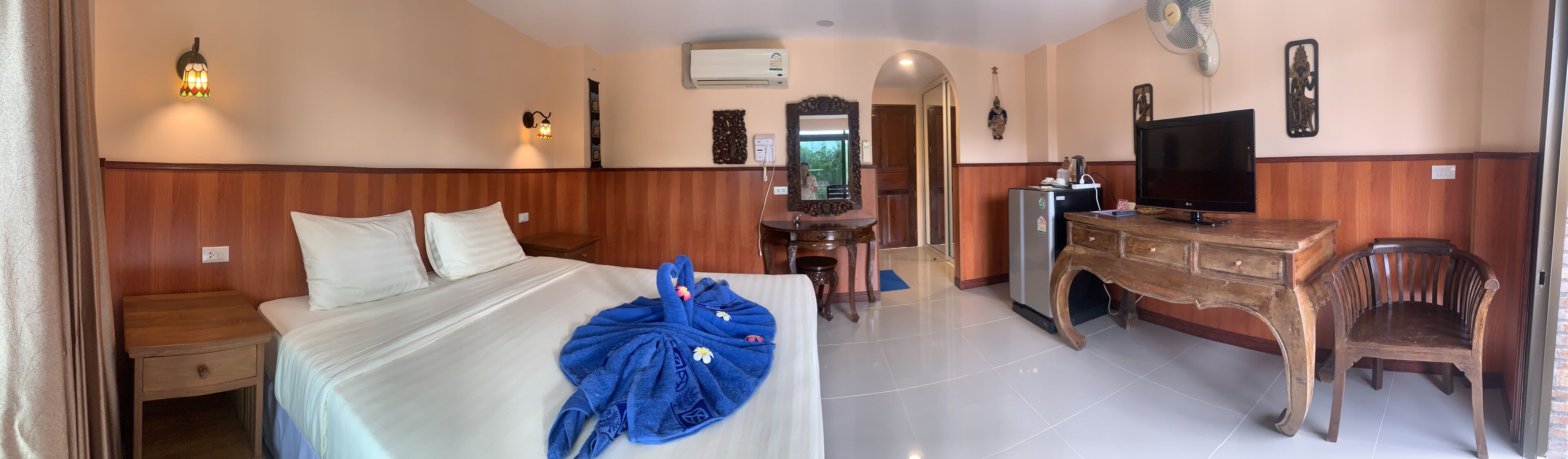 Habitación de hotel con cama, mesita de noche, cómoda, televisor y espejo.