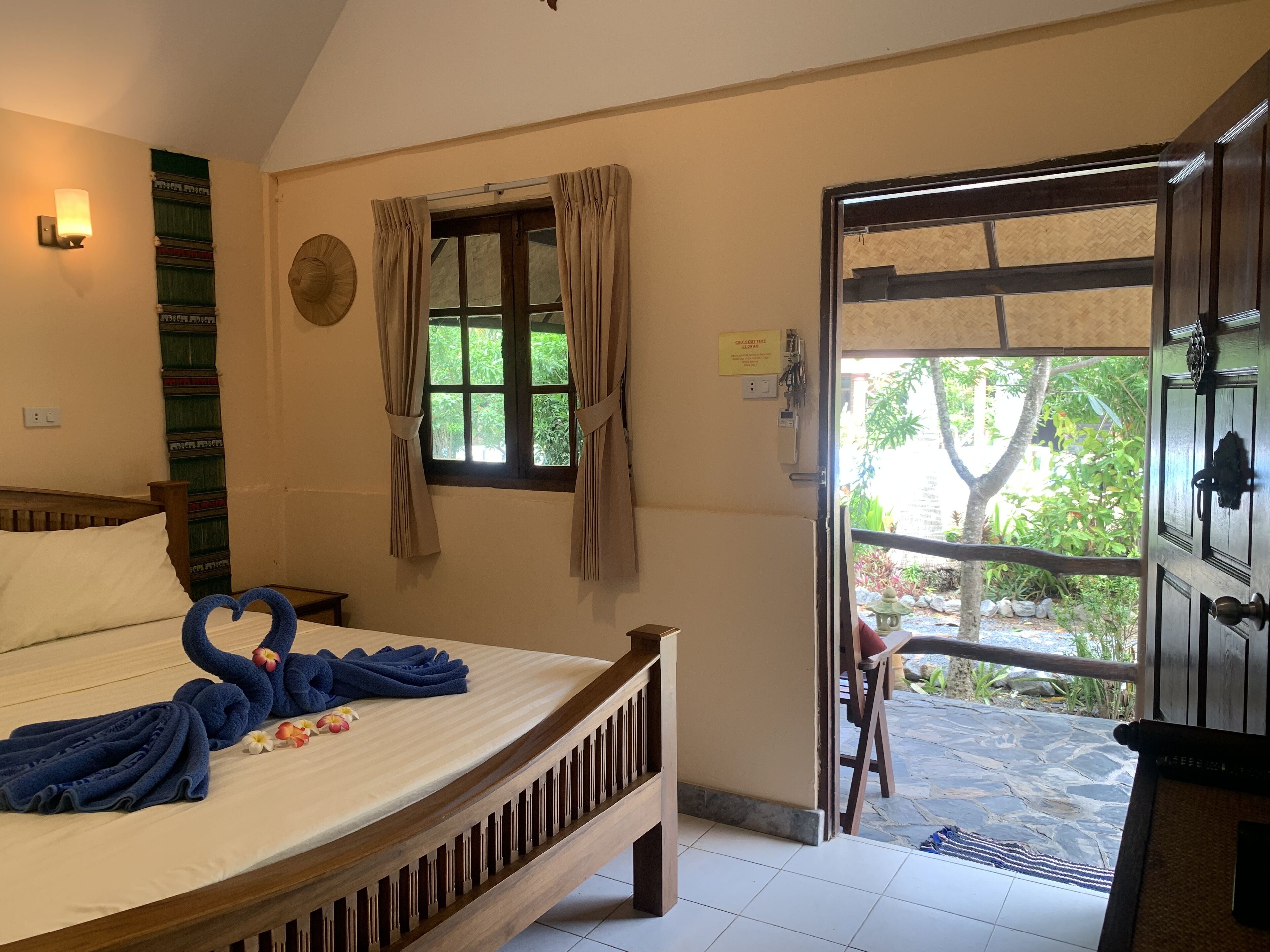 A bedroom with a bed, a window with curtains, a wall-mounted light, and a door leading to an outdoor area.