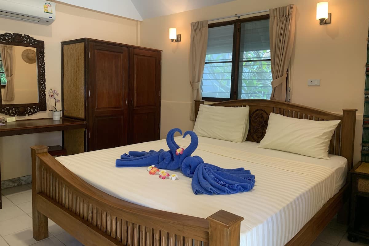 A neatly made bed with blue towels and a heart-shaped decoration, a wooden wardrobe, a mirror, and a window with curtains.
