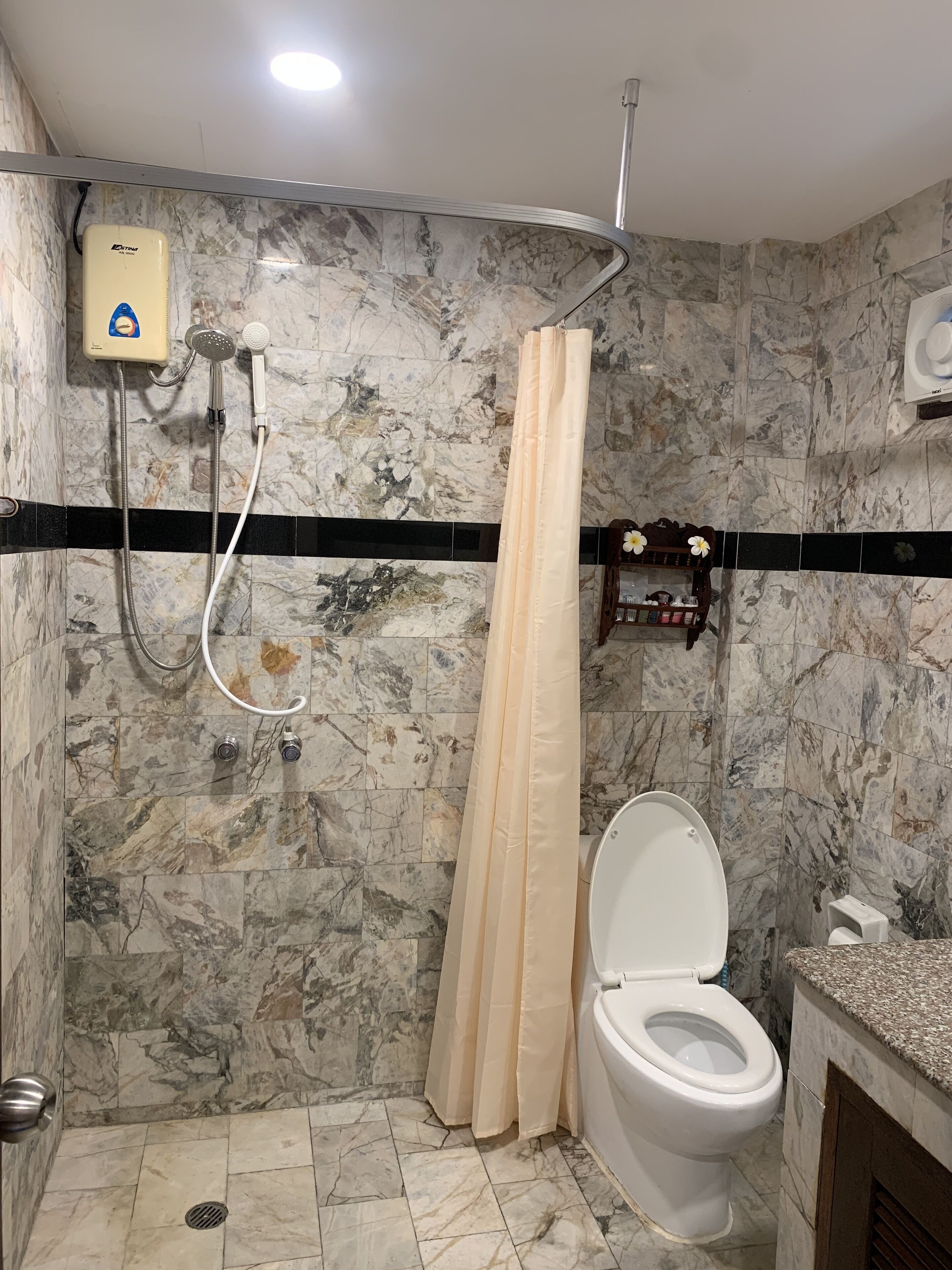A bathroom with a shower, toilet, and marble walls.