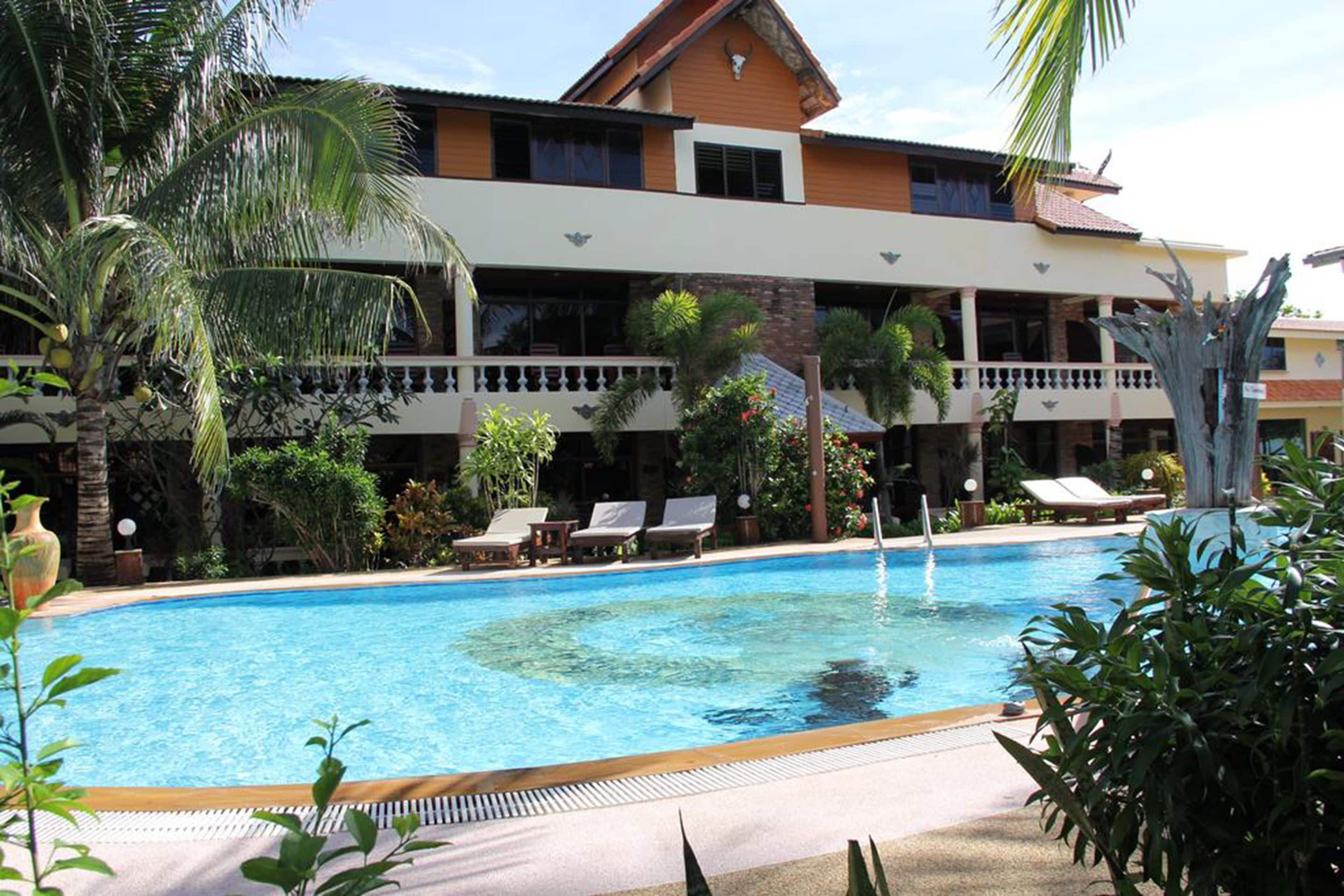 Ein Hotel mit Swimmingpool, Liegestühlen und Palmen.