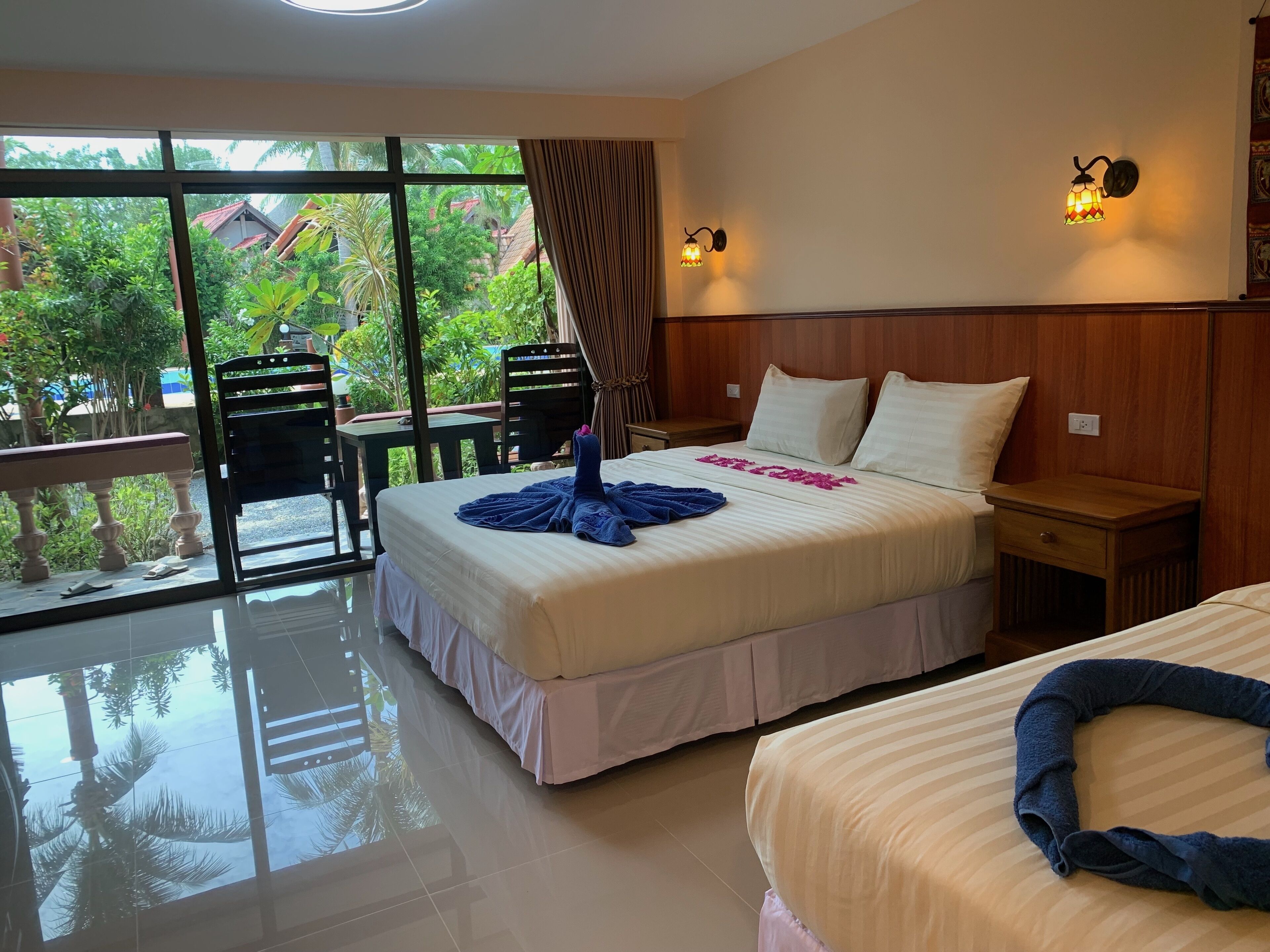 Habitación de hotel con un ventanal grande, una cama con una toalla azul, una mesita de noche y un cabecero de madera.