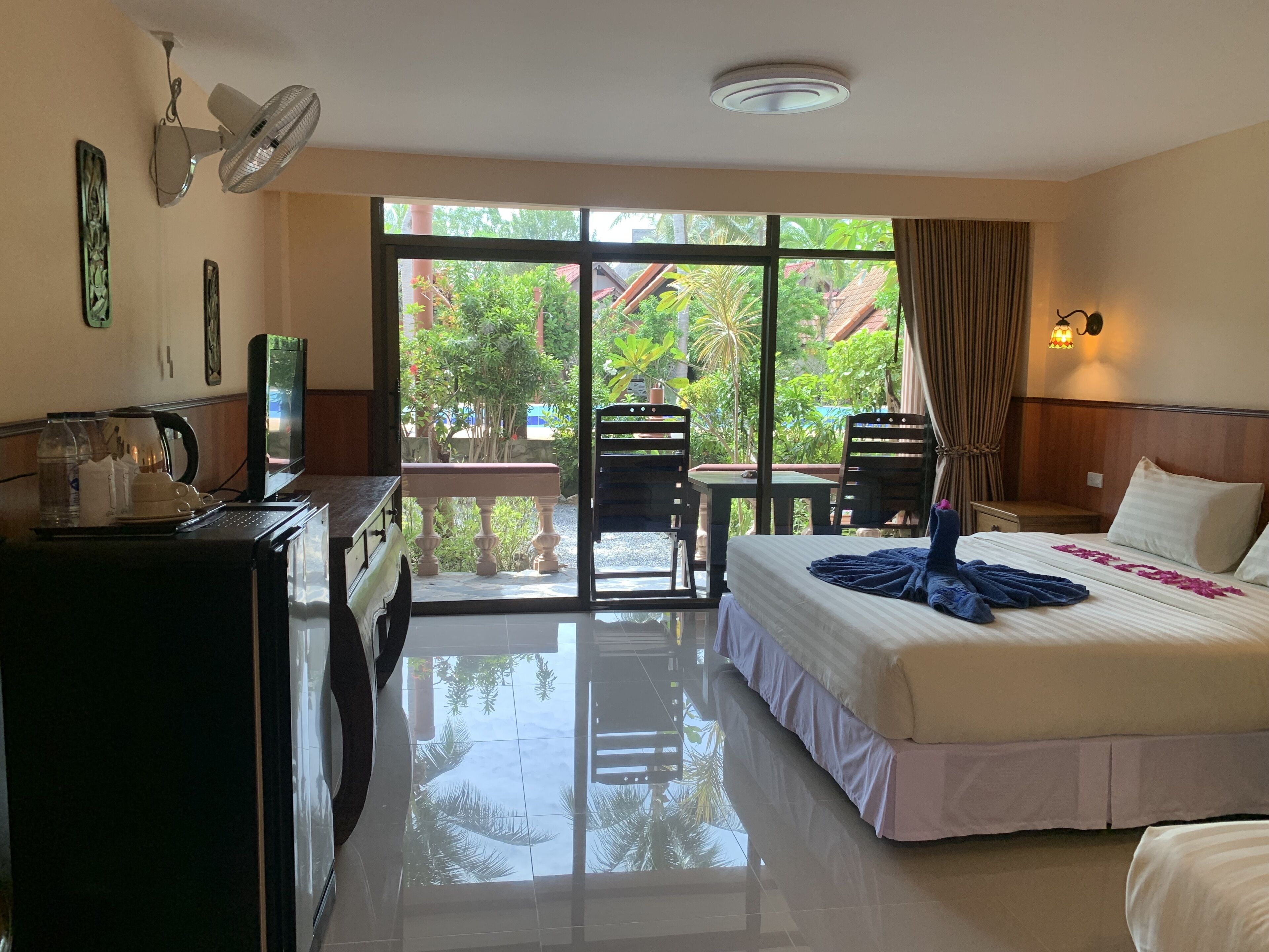 A hotel room with a bed, a desk with a coffee maker, a TV, and a balcony with chairs.