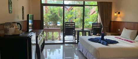 A hotel room with a bed, a desk with a coffee maker, a TV, and a balcony with chairs.