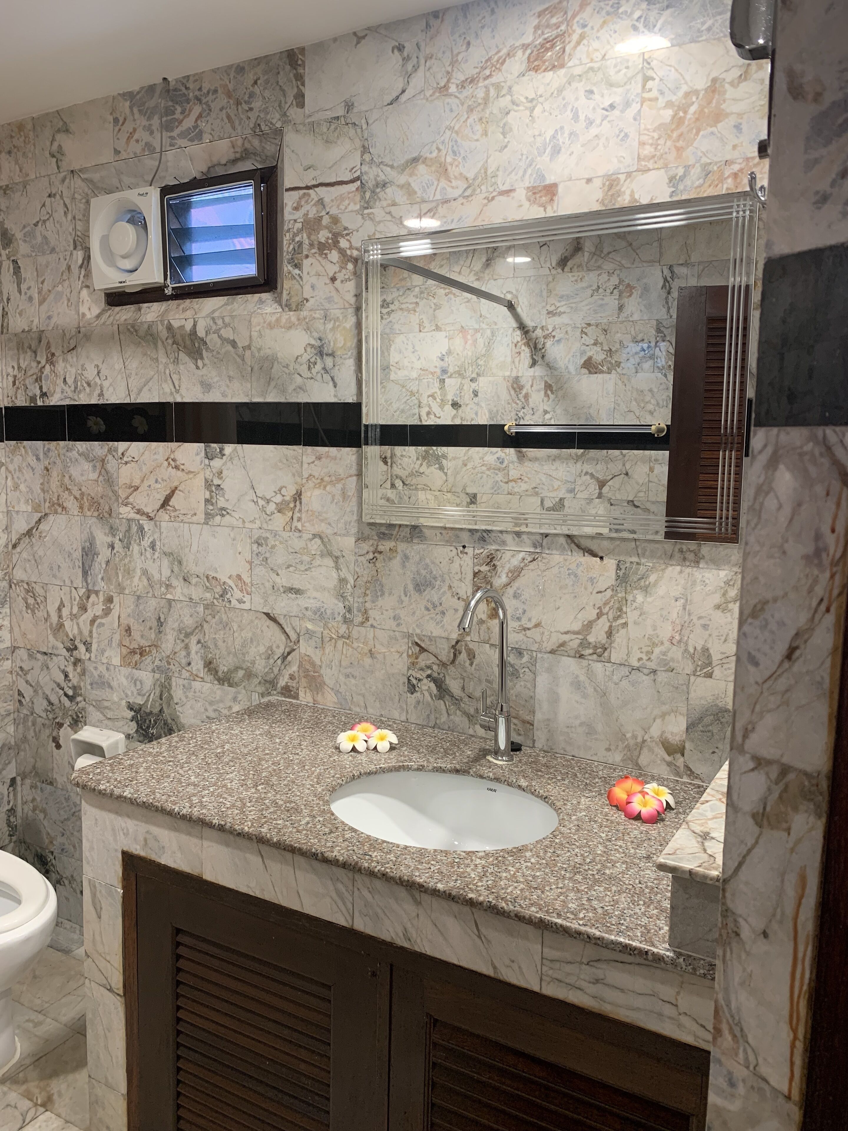 A bathroom with a marble wall, a built-in sink, a mirror, and a ceiling fan.