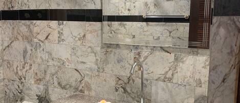 A bathroom with a marble wall, a built-in sink, a mirror, and a ceiling fan.