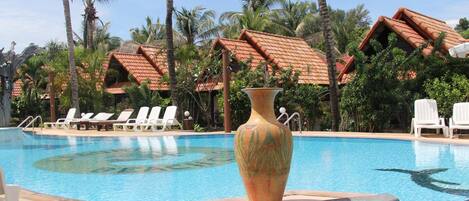 A pool area with lounge chairs, a large decorative vase, and buildings with red-tiled roofs.
