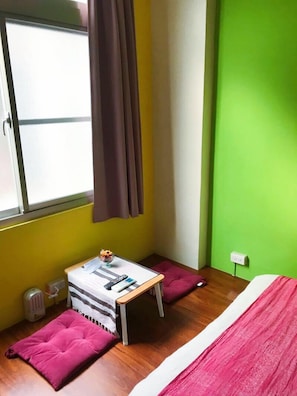 Una habitación con una cama, una mesita con un control remoto, una ventana con cortinas y una pared verde.