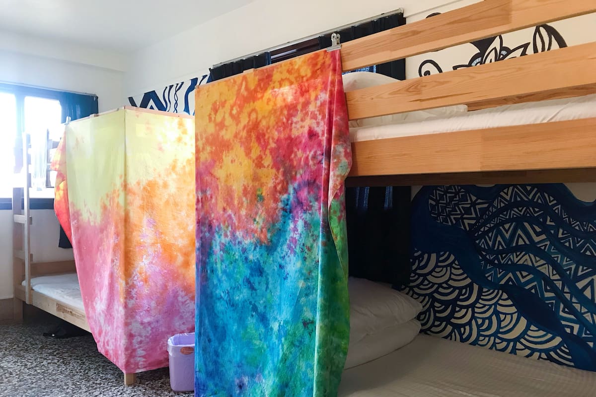 A bunk bed with colorful tie-dye curtains, a patterned pillow, and a small trash bin.