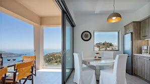 A modern kitchen with a view of the sea, a dining area with white chairs, and a large window. - Sellia Resort (Agios Vasileios)