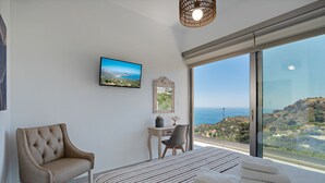 A bedroom with a large bed, a chair, a desk, a television, and a view of the sea. - Sellia Resort (Agios Vasileios)
