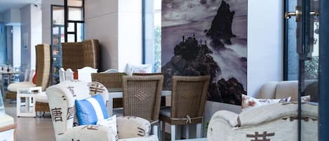 A modern hotel lobby with wicker furniture, a large wall mural, and a view of the outdoors.