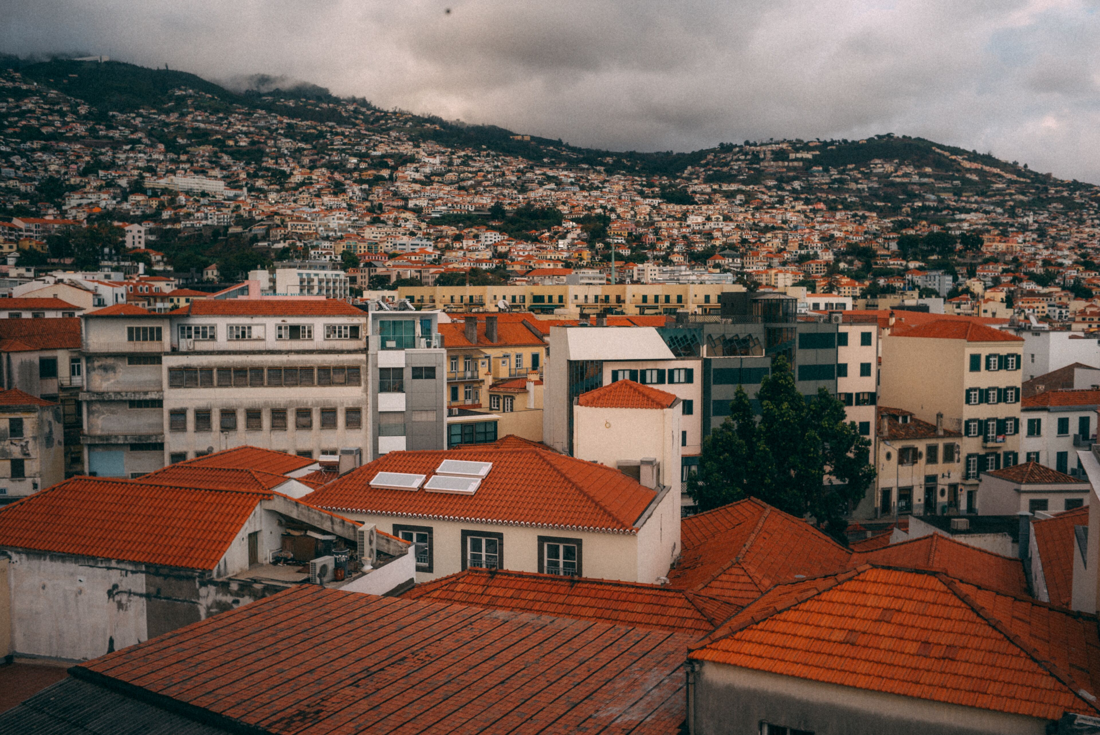 Un paysage urbain caractérisé par un quartier résidentiel densément peuplé, des bâtiments aux toits recouverts de tuiles rouges et un arrière-plan vallonné.