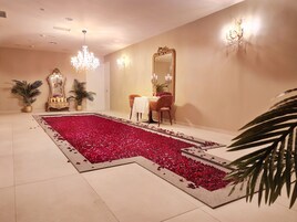 A room with a large red flower petal carpet, a chandelier, a mirror, and a table with candles.