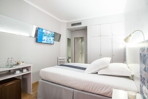 A modern hotel room with a bed, a TV mounted on the wall, a desk with a chair, and a wardrobe.