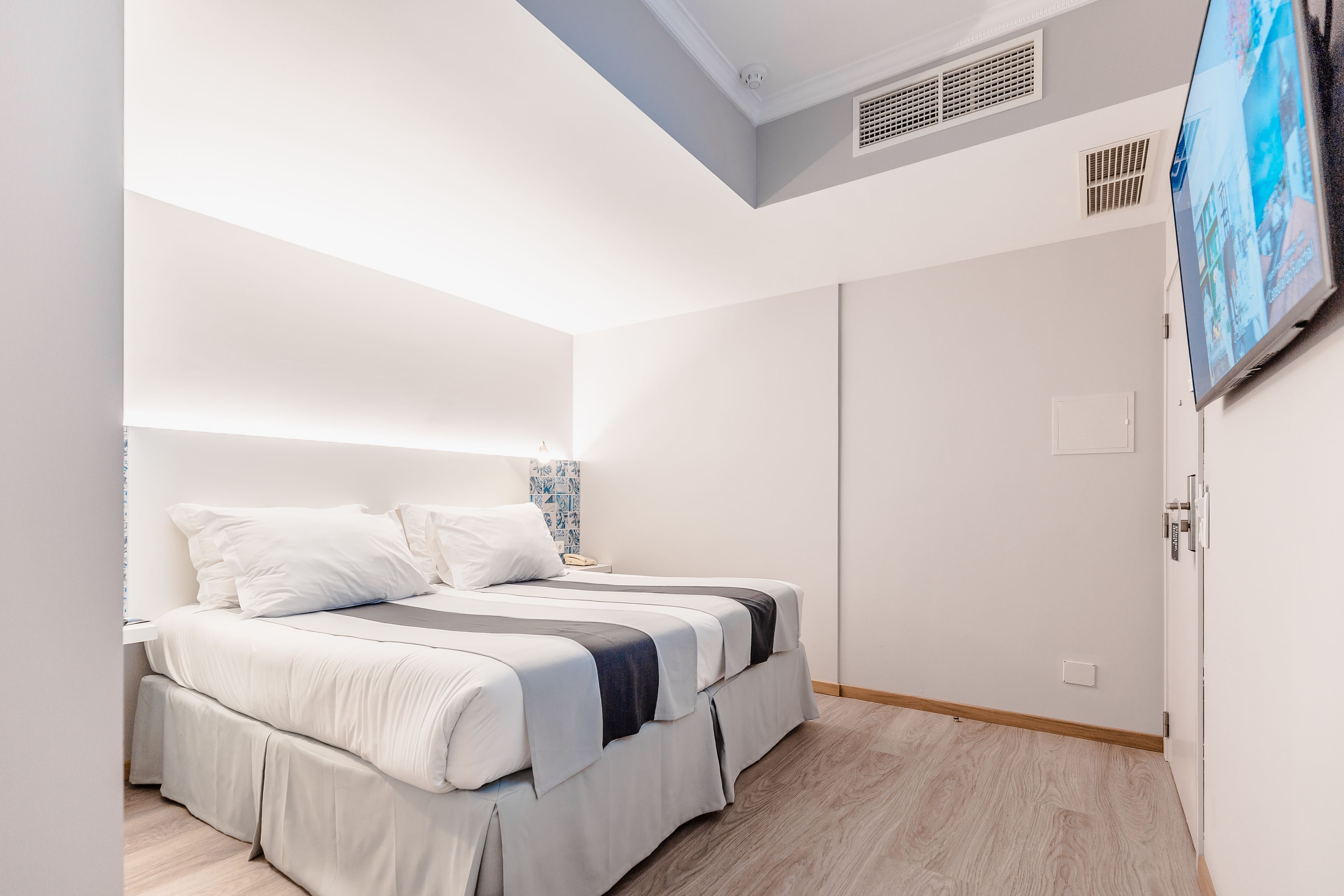 A modern bedroom with a bed, a TV mounted on the wall, and a door.