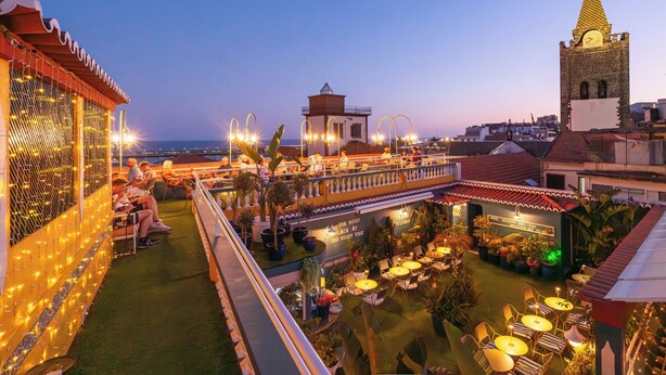An outdoor rooftop terrace with seating areas, potted plants, and a view of a cityscape including a church tower. - Sé Boutique Hotel (Funchal)