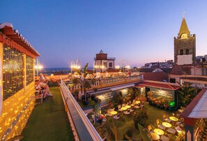 An outdoor rooftop terrace with seating areas, potted plants, and a view of a cityscape including a church tower. - Sé Boutique Hotel (Funchal)