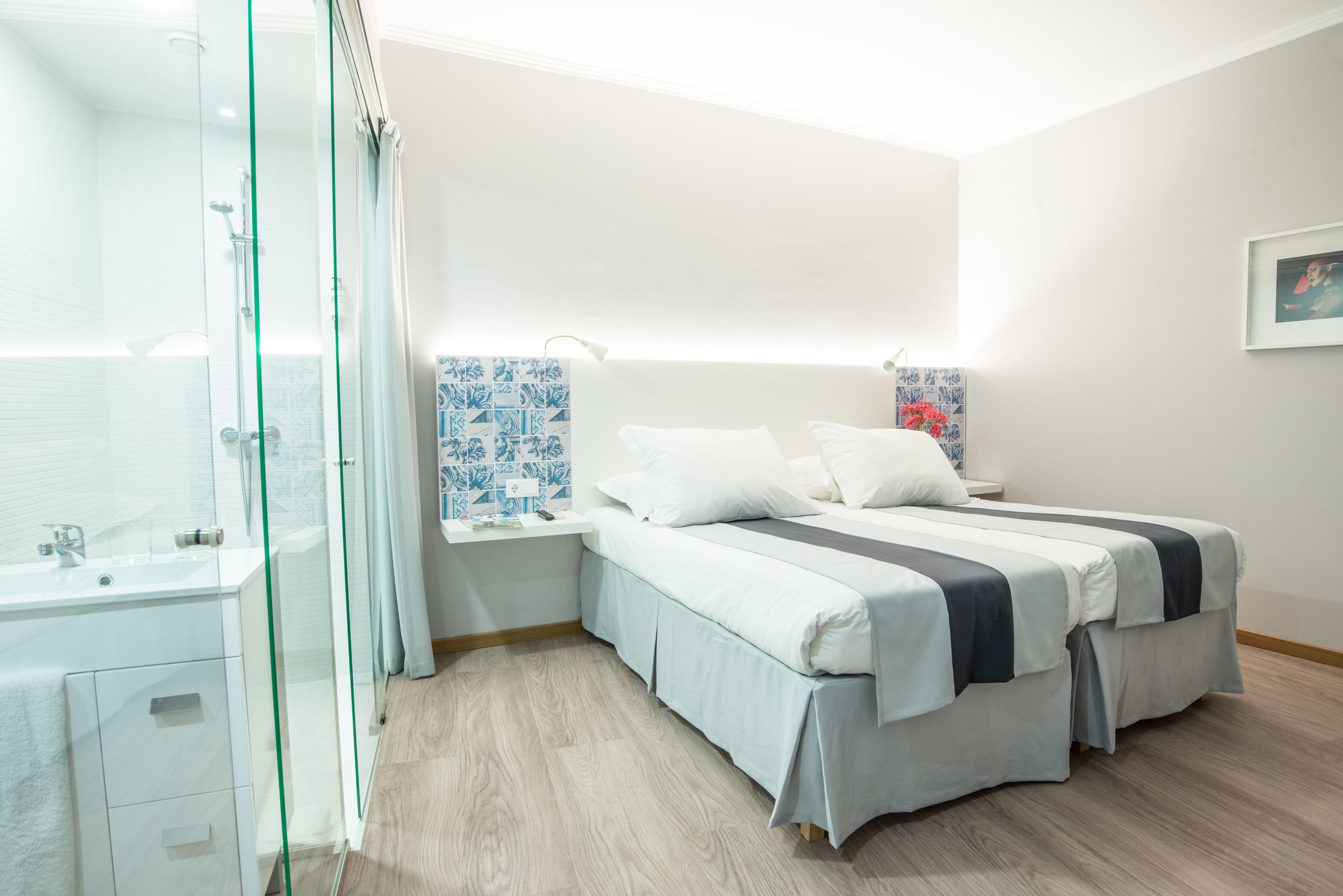 Une chambre moderne avec une douche en verre, une table de chevet blanche, un lit avec deux oreillers et un mur à motifs bleus.