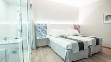 Un dormitorio moderno con cabina de ducha de vidrio, una mesita de noche blanca, una cama con dos almohadas y una pared con estampado azul.