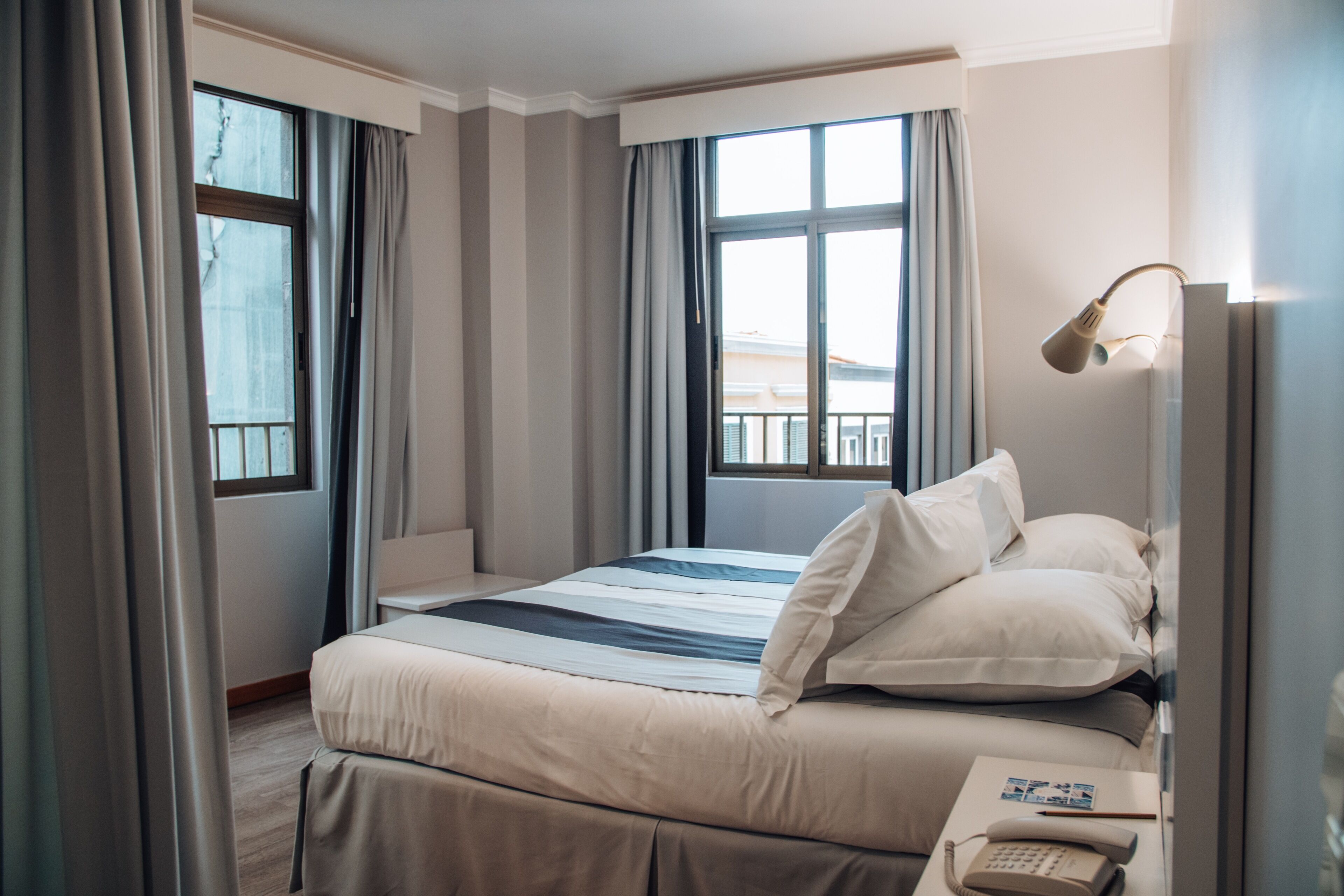 A hotel room with a bed, curtains, a bedside lamp, and a phone on the nightstand.