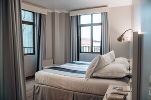 A hotel room with a bed, curtains, a bedside lamp, and a phone on the nightstand.