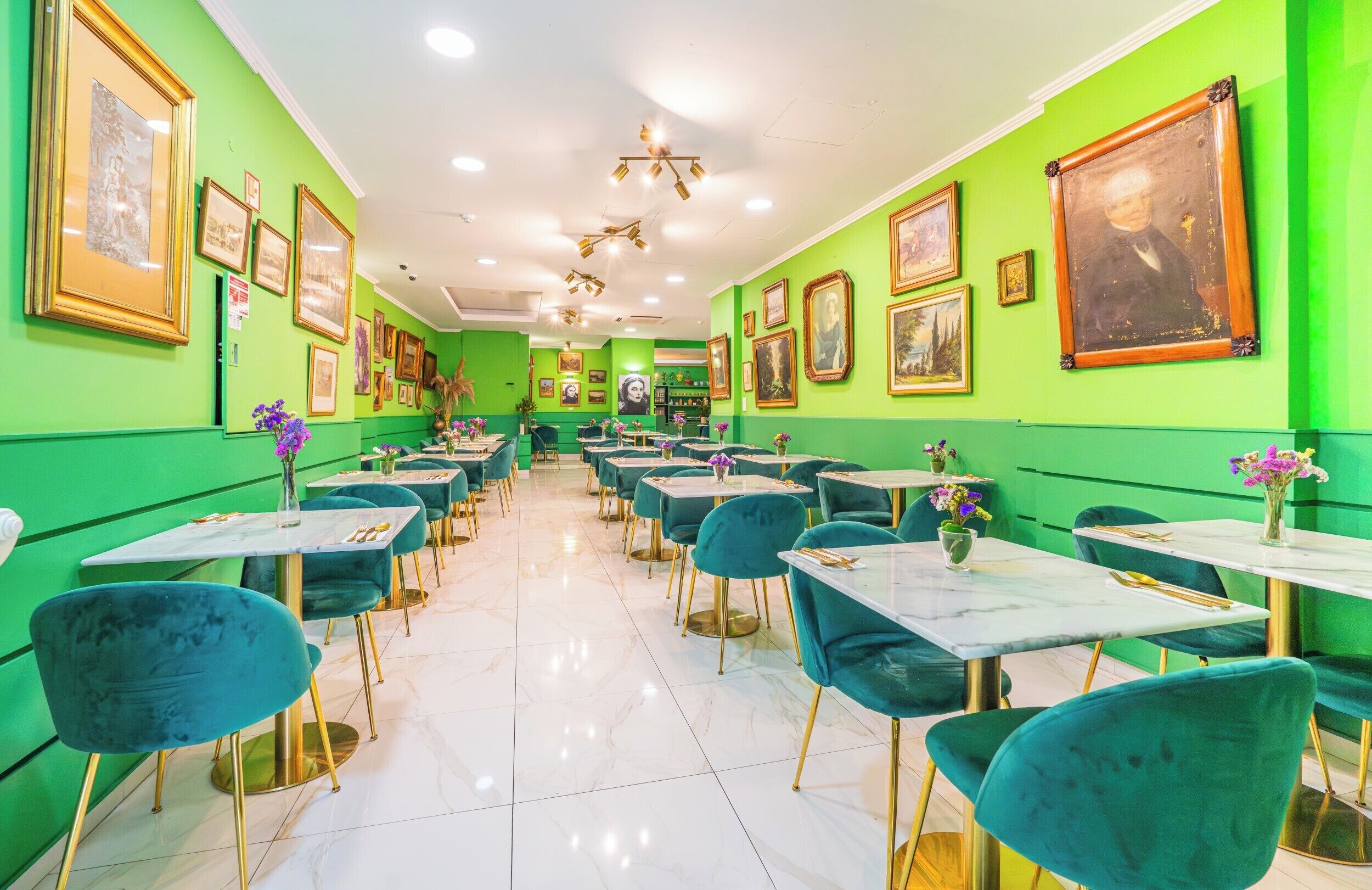 Un restaurante con paredes verdes, pisos de mármol y sillas color turquesa. Las mesas están cubiertas con manteles blancos y sillas doradas.