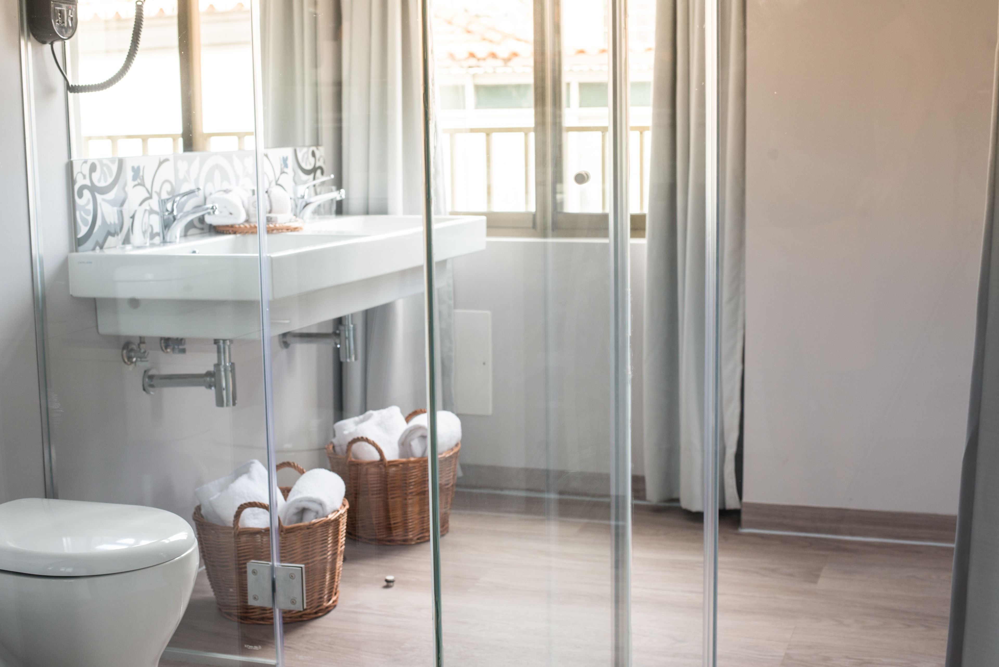 Een badkamer met een douchecabine van glas, een witte wastafel en twee rieten manden met handdoeken.